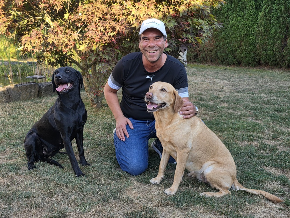 Oliver Maiß, Mitarbeiter bei Pudelwohl365, mit zwei Labradoren im Garten